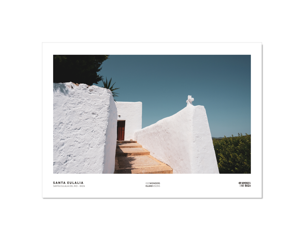 Photographic print featuring Mediterranean white washed walls with a church cross at one corner, blue sky and surrounding foliage.